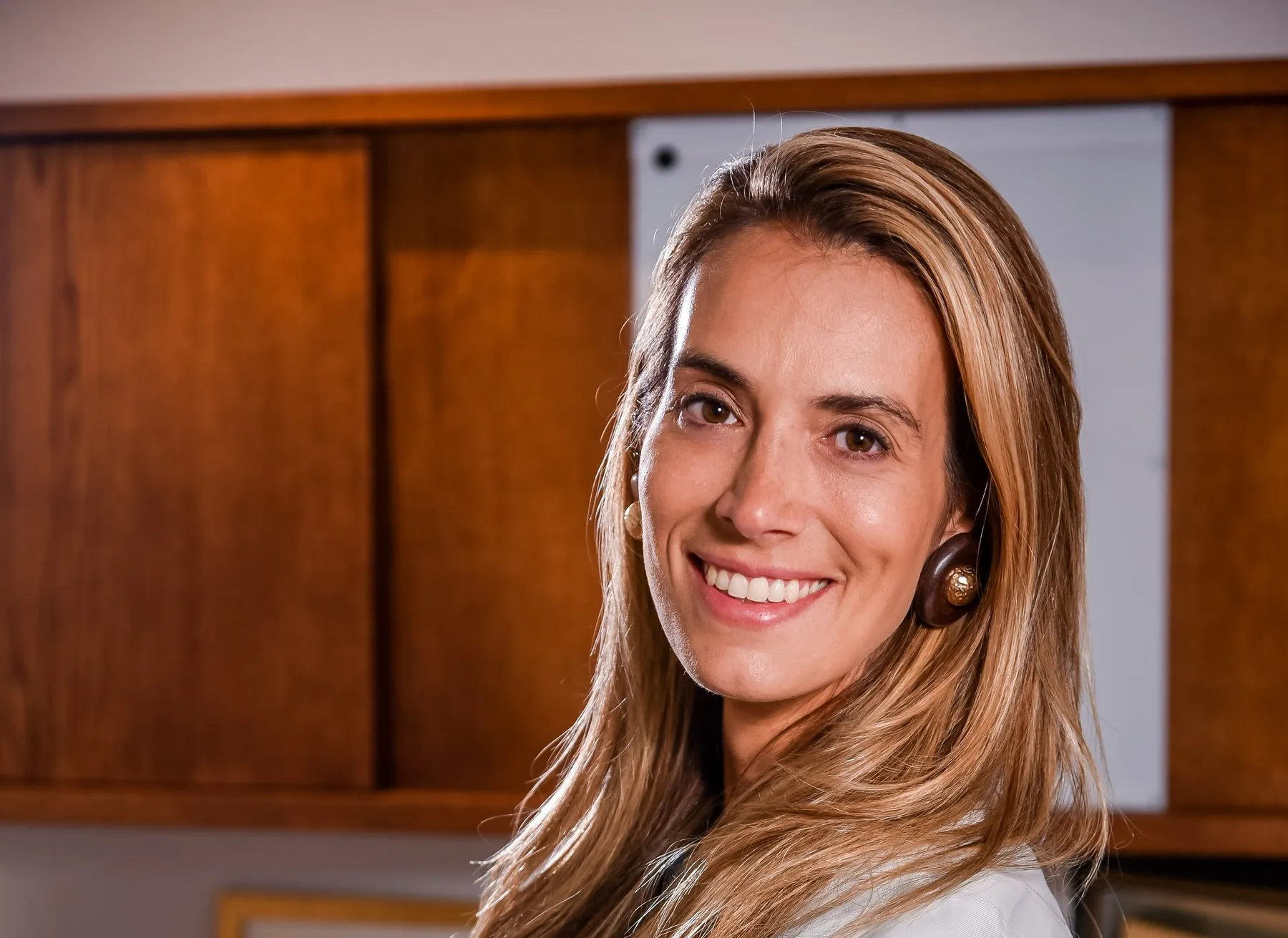 Dra. Raquel Stamm, de jaleco, sorrindo em seu consultório