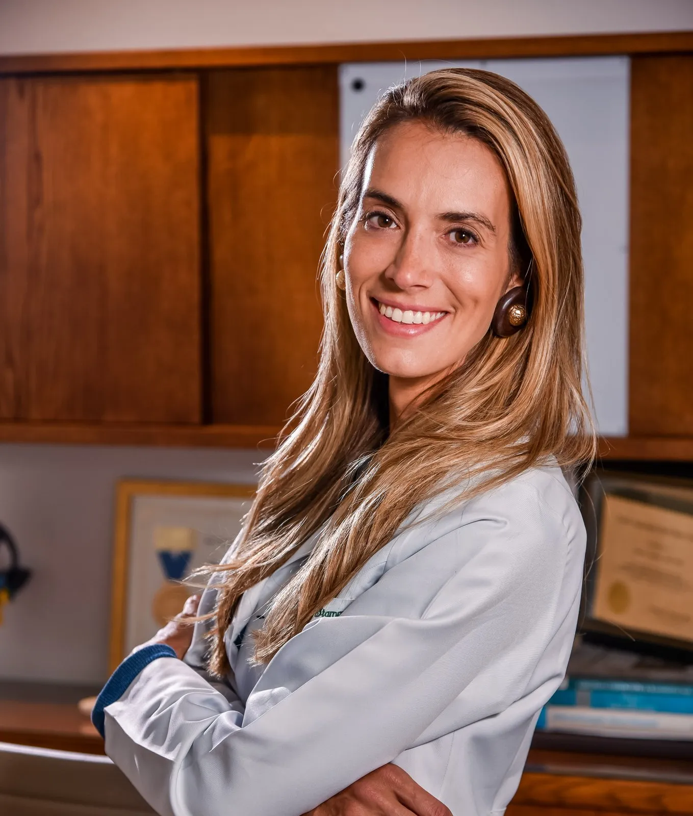 Retrato da Dra. Raquel Stamm, de jaleco, de braços cruzados em seu consultório